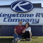 Keystone Ambassadors Jimmy & Lisa Cox of FindUsCamping sitting in front of Keystone RV sign
