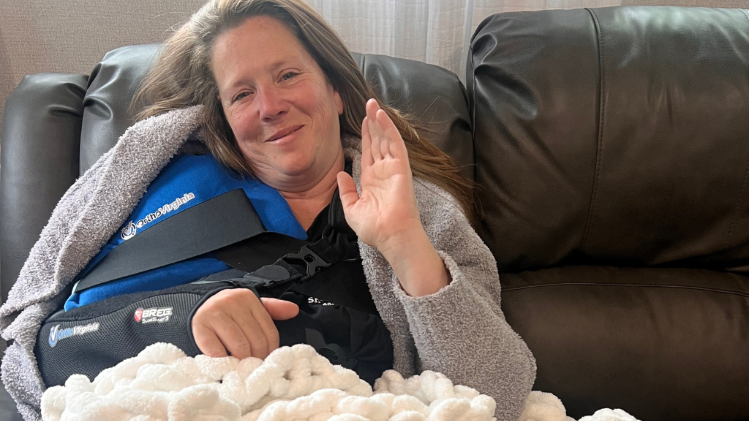 Image of Lisa sitting on the couch the day after rotator cuff surgery. She is wearing a sling on her right arm. This is a photo of Lisa, the author's wife, sitting on the couch the day after her rotator cuff surgery. She is wearing a sling on her right arm to support her shoulder. She is looking tired but happy to be home and recovering.