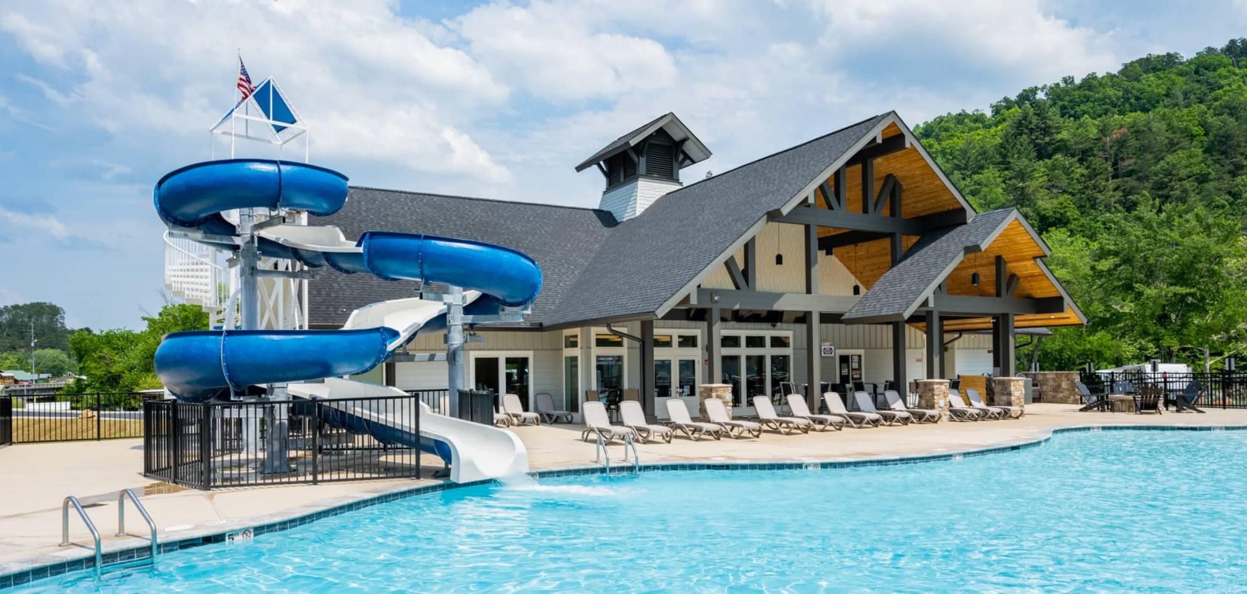 Pigeon Forge RV Resort clubhouse and pool. Two-story building with large pool in foreground. The water slide has water coming down it