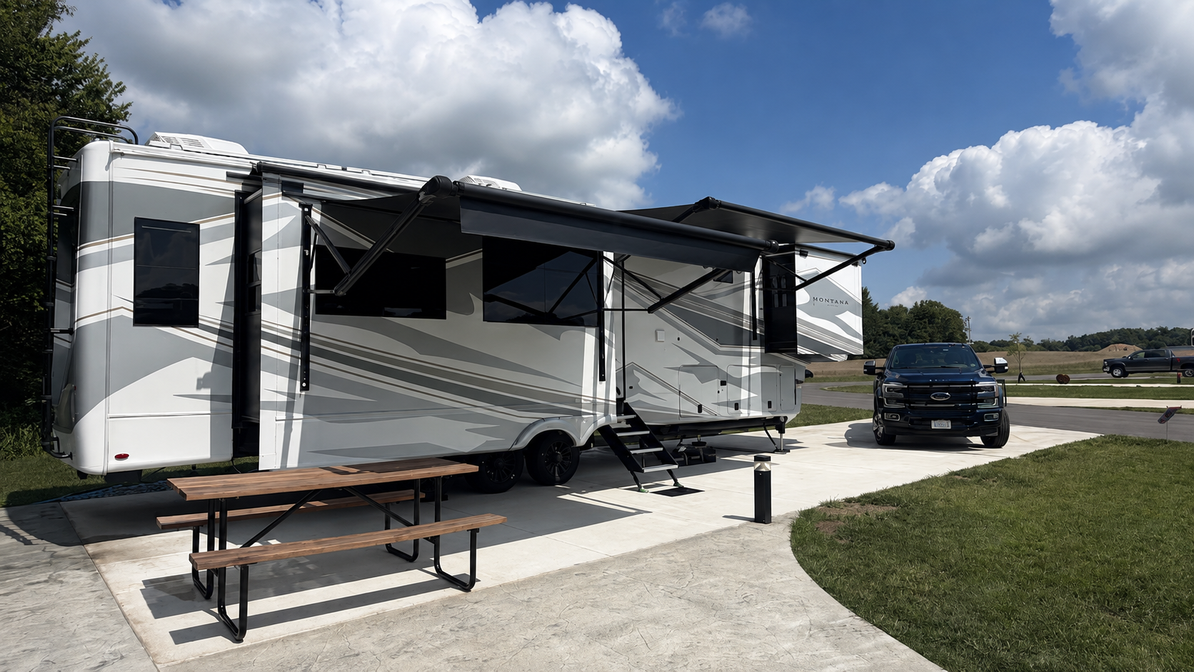The FindUsCamping Montana set up at a campground with its awning open beside the Ford F-450