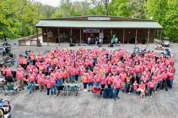 Aerial photo of FindUsCamping Villagers in matching pink shirts gathered for a group photo at an RV campout