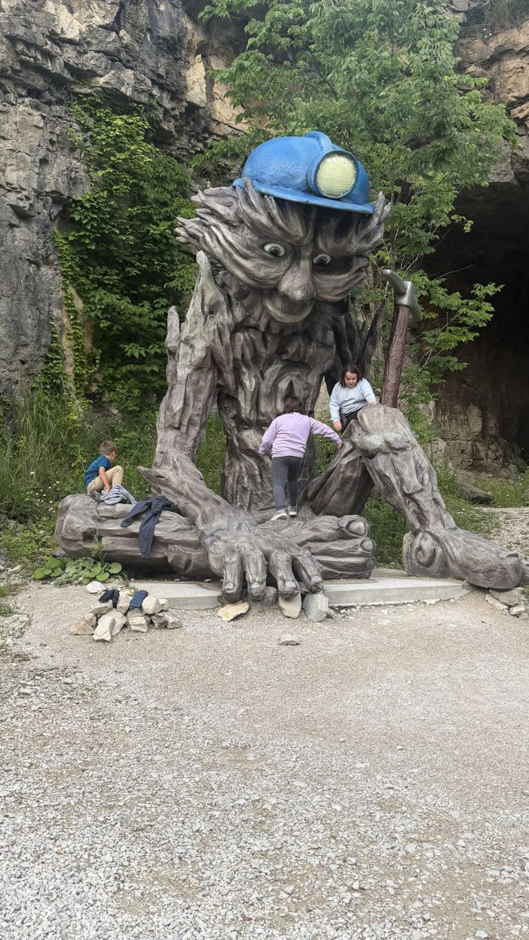 Kids climbing a giant miner troll statue outside the cave