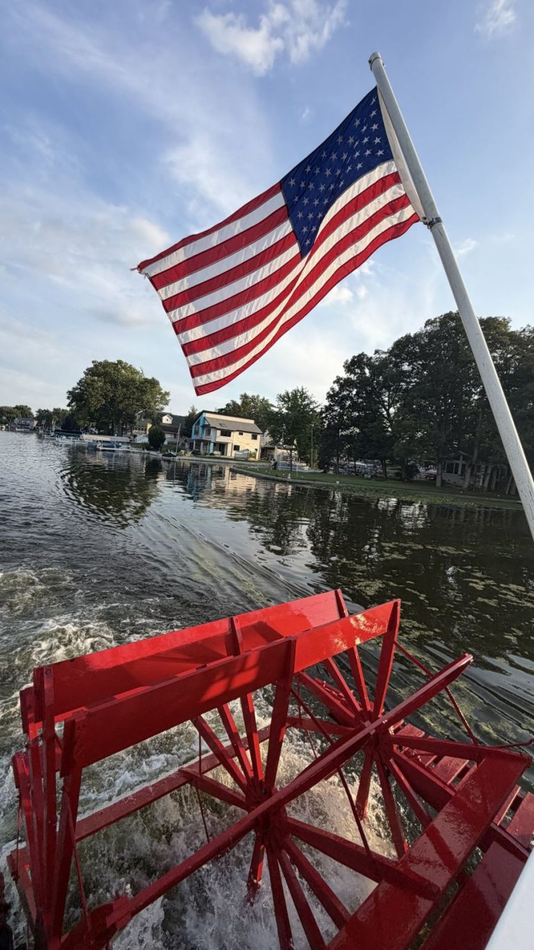 American flag over a red paddlewheel on a lake boat ride
